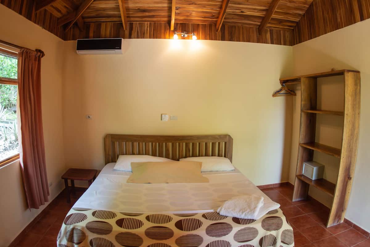 A bedroom with a wooden ceiling, a bed with patterned bedding, a ceiling fan, and a window with curtains.