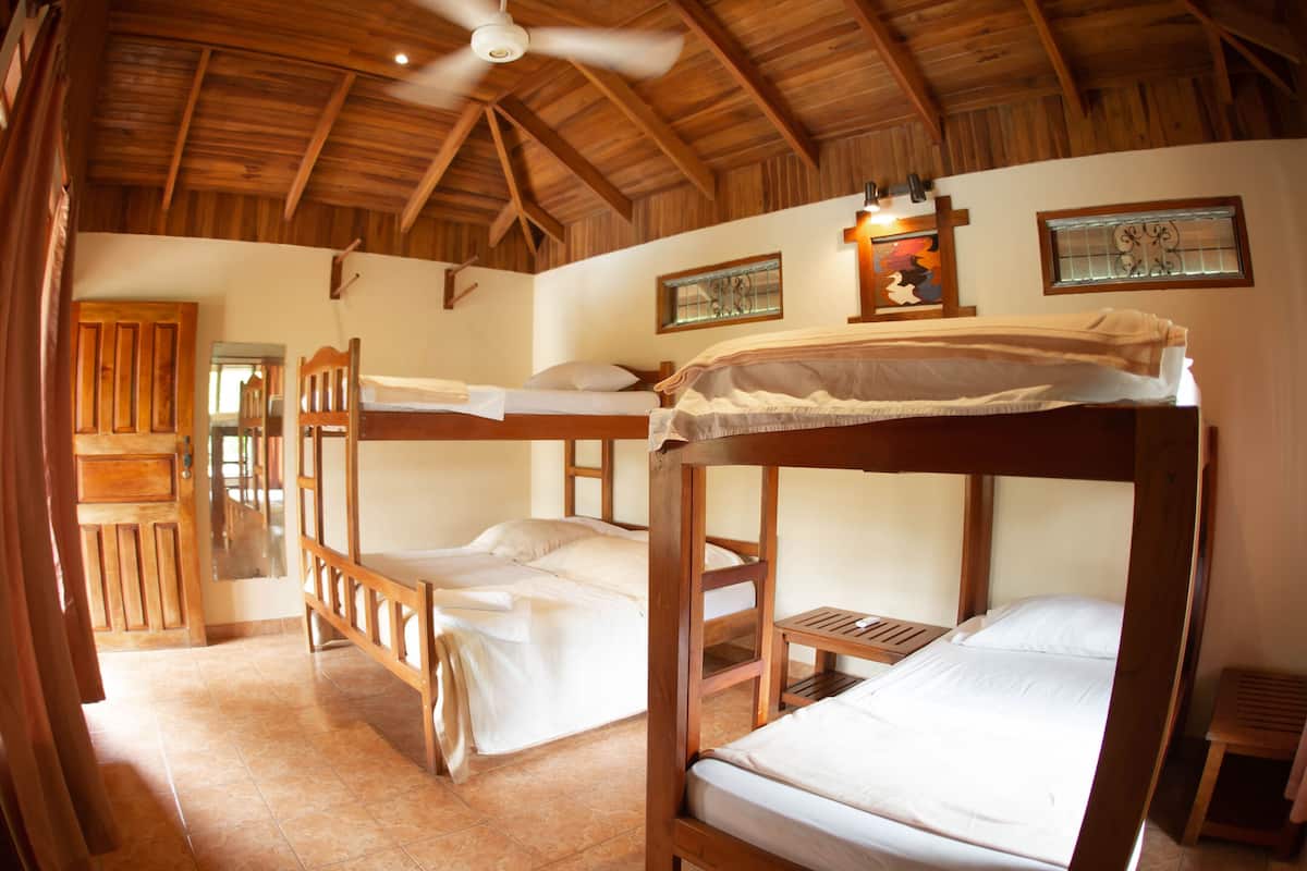 A room with two bunk beds, wooden beams on the ceiling, a ceiling fan, and a small table.