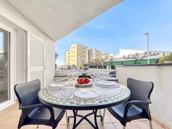 A round table with two chairs, a tiled floor, and a view of buildings in the background. - Platja de Roses by Interhome (Roses)
