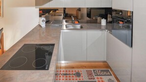 A modern kitchen with white cabinets, a built-in oven, a stovetop, and a dining area with a menu placemat. - Blauherd by Interhome (Zermatt)