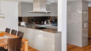 A modern kitchen with a central island, white cabinetry, and a dining area with a wooden table and chairs. - Blauherd by Interhome (Zermatt)
