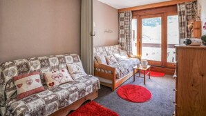 A cozy room with a sofa and a bed, a wooden cabinet, and a window with curtains.