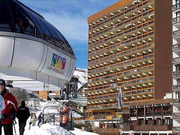 A modern building with a grid of balconies, a ski lift, and a sign for "Les Sybbles".