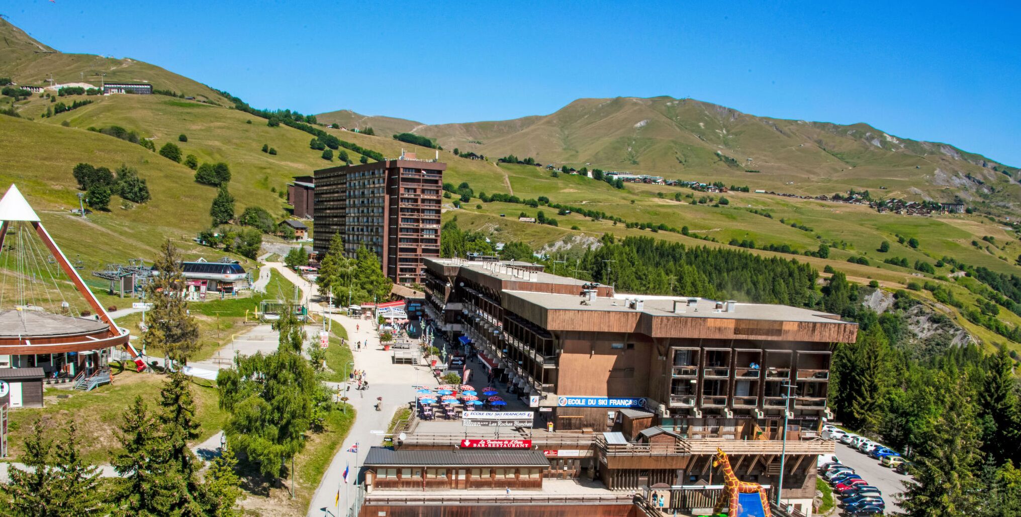 A hotel with multiple floors, outdoor seating, and a view of surrounding hills.