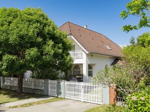 Une maison à deux étages, avec une façade blanche, un toit brun et une clôture blanche faite de piquets.