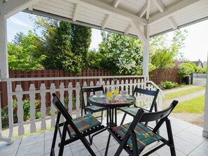 Une terrasse couverte avec une clôture blanche, une table avec des chaises et un magazine.