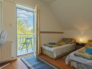 A bedroom with two beds, a fan, and a view of a balcony with a chair.