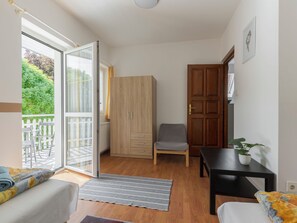 Une chambre comprenant un lit, une chaise, une table, une armoire et une porte-fenêtre coulissante donnant sur un espace extérieur avec un balcon.