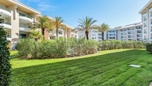 A hotel courtyard with neatly trimmed grass, palm trees, and a row of white buildings with balconies. - Le Cesarée by Interhome (Fréjus)