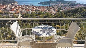 Un balcón con sillas de mimbre y una mesa, con vistas a un pueblo costero, edificios y el mar.