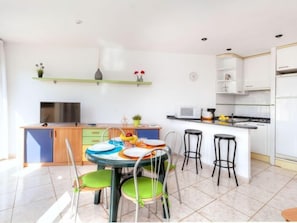 Une cuisine moderne avec des meubles blancs, un four à micro-ondes et un évier. On y trouve également un coin repas avec une table ronde et des chaises colorées.