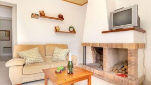 Ein Wohnzimmer mit einem beigen Sofa, einem Holztisch, einem Kamin und einem Fernseher auf einem Schrank.