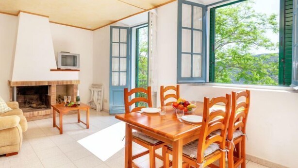 Ein gemütliches Wohnzimmer mit Kamin, einem Esstisch mit Stühlen und einem großen Fenster mit grünen Fensterläden.