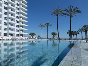 Um hotel moderno com área de piscina, palmeiras e céu azul.