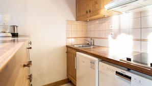 Una cocina compacta con armarios de madera, un lavaplatos integrado y electrodomésticos blancos.