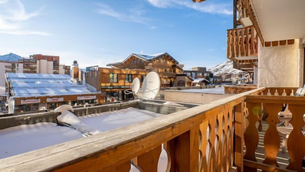 Un balcón de madera con vista a una montaña nevada y edificios al fondo.