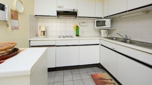 Una cucina compatta con mobili bianchi, un forno a microonde, una macchina da caffè e un lavello.