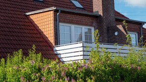 Een bakstenen huis met een rode dakbedekking, twee dakramen, een schoorsteen en een witte hek met beplanting ervoor.
