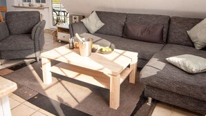 Een knusse woonkamer met een grijze bank, een houten salontafel en een klein bijzettafeltje.