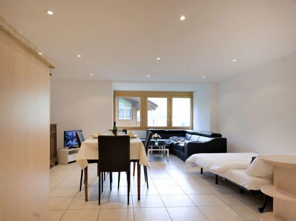 A modern, well-lit room with a dining table, a sofa, and a bed.