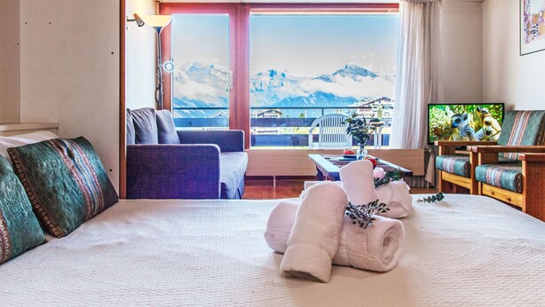 A hotel room with a large bed, a sofa, a TV, and a balcony with a mountain view. - Christiania 2 O3 by Interhome (Nendaz)