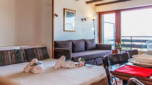 A hotel room with a bed, a sofa, a dining table with plates and a red napkin, a window with a view, and a painting on the wall. - Christiania 2 O3 by Interhome (Nendaz)