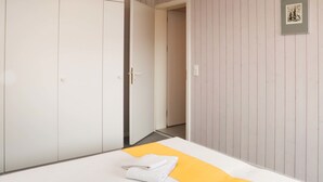 Quarto com cama, guarda-roupa e porta que dá para outro cômodo.