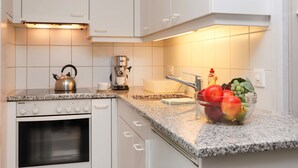 Cozinha moderna com armários brancos, forno embutido, cafeteira e uma fruteira no balcão.