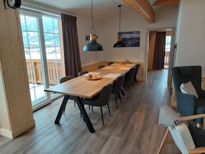 A modern dining area with a wooden table and chairs, large windows with curtains, and a view of the mountains.