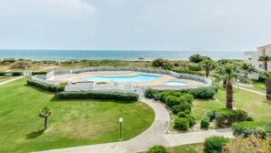A pool area with a view of the ocean, surrounded by well-maintained lawns and palm trees. - Les Goelettes by Interhome (Saint Cyprien)