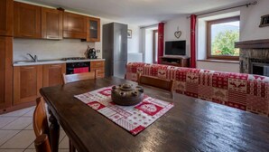Een gezellige keuken met houten kastjes, een eettafel met een tafelkleed met patroon en een open haard.
