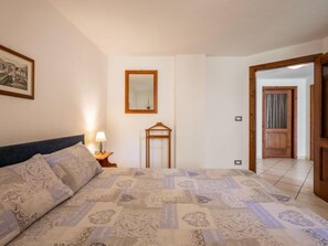Un dormitorio con cama, una mesita de noche con lámpara, un espejo y una puerta que da a otra habitación.