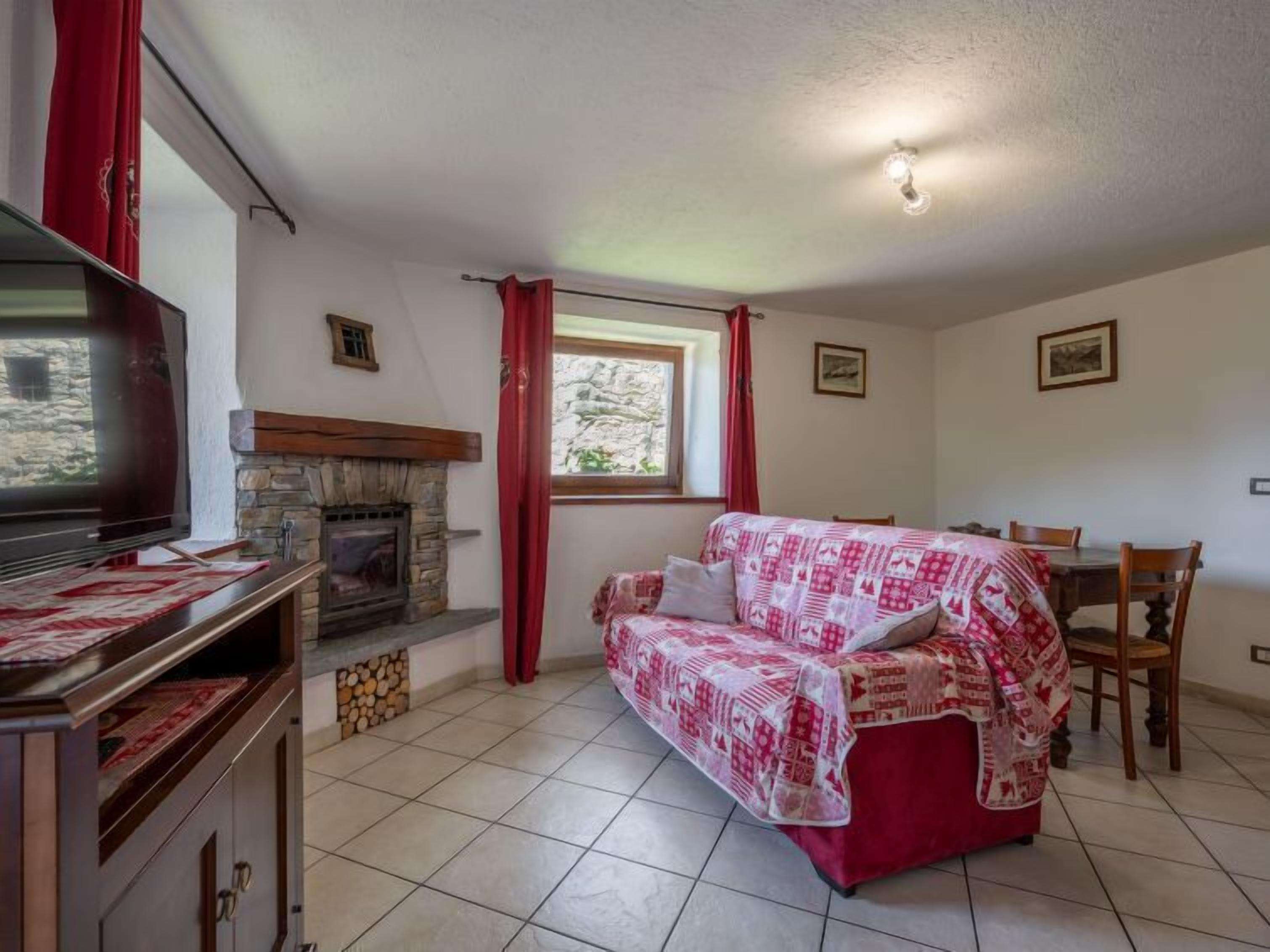 A cozy living room with a stone fireplace, a television, a red and white patterned sofa, and a dining area with a table and chairs.