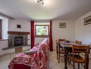 Una habitación acogedora con chimenea de piedra, un sofá con una manta estampada, una mesa de comedor con sillas y una ventana con vistas a la vegetación.