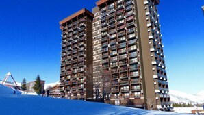 Un edificio de gran altura con múltiples balcones, un telesilla al fondo y un cielo azul despejado.