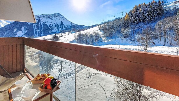 Vista de la montaña desde un balcón con baranda de madera, una mesa con cesta de frutas y cielo despejado.
