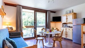 Una habitación acogedora con un sofá azul, sillas de madera, una mesa de comedor y una zona de cocina con armarios y un refrigerador.