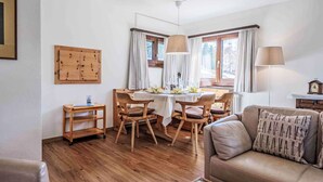 Un salon chaleureux avec un plancher en bois, un canapé en cuir marron, une table à manger avec des chaises et un buffet en bois accroché au mur.