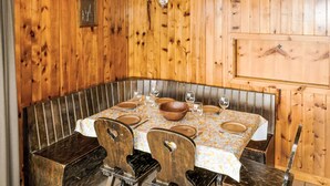 A wooden-paneled room with a table set for four, including a wooden bench, four chairs, and a hanging light fixture.