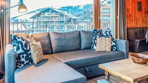 A modern living room with a sectional sofa, a wooden coffee table, and large windows offering a view of a mountain resort.