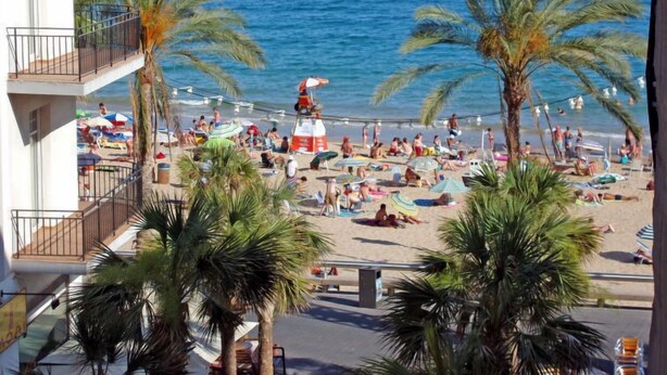 Una playa con palmeras, una torre de salvavidas y gente relajándose.