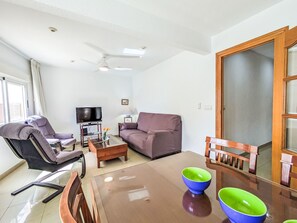 Een woonkamer met een bank, fauteuil, televisie, salontafel en een eettafel met stoelen.