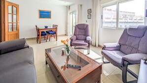 Una sala de estar con un sofá, dos sillones, una mesa de centro, una mesa de comedor con sillas, un cuadro y una ventana con vistas.