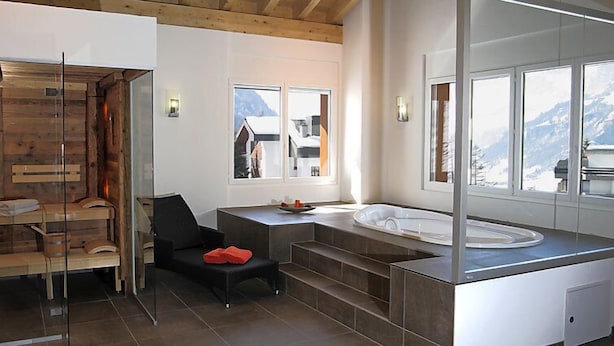 A modern bathroom with a wooden ceiling, a bathtub, a glass shower enclosure, and a view of mountains.