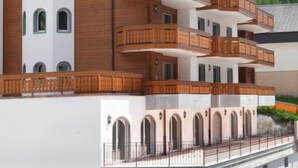 A multi-story hotel with balconies, a white facade, and a mountainous backdrop.
