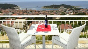 Un balcon avec des fauteuils en osier et une table, d’où l’on a vue sur une ville côtière, avec ses bâtiments et la mer.
