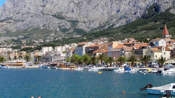 Une ville côtière avec des bâtiments, un port de plaisance et une chaîne de montagnes en arrière-plan.