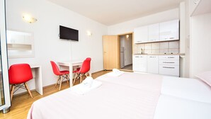 Une chambre d’h ôtel avec un lit, un bureau avec deux chaises rouges, une télévision et une kitchenette.