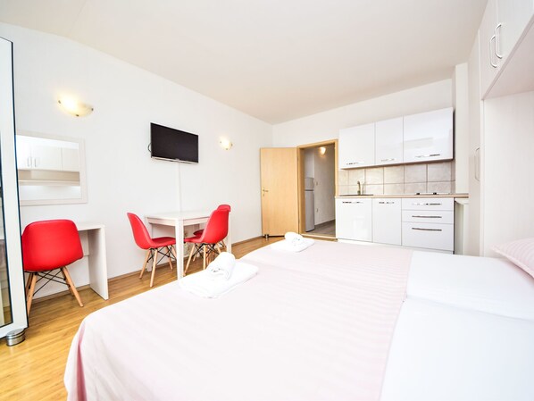 Une chambre d’hôtel avec un lit, un bureau avec deux chaises rouges, une télévision et une kitchenette.