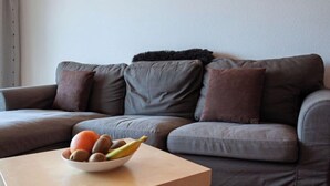 Un salón moderno con un sofá gris, dos luces empotradas en la pared y un frutero sobre una mesita.